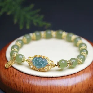 Hetian jade lotus beaded bracelet with 14K gold accents displayed on wooden base with green foliage background