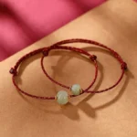 Hetian jade lotus red string bracelet flat lay with braided red-gold cord and carved jade bead on craft paper background