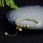 Light green Hetian jade lotus bracelet displayed overhead on dark blue ceramic tray with natural foliage
