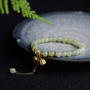 Light green Hetian jade lotus bracelet displayed overhead on dark blue ceramic tray with natural foliage