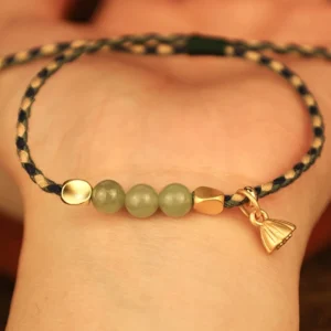 Handcrafted jade lotus charm bracelet held in palm showing close-up detail of braided cord and gold pendant