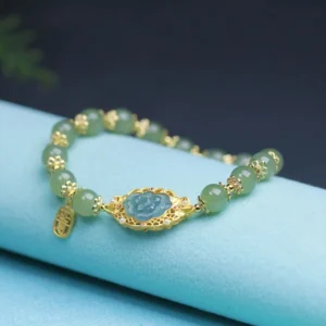 Close-up side view of authentic Hetian jade bracelet showing polished green jade beads, sterling silver spacers, and blue lotus charm on light blue fabric