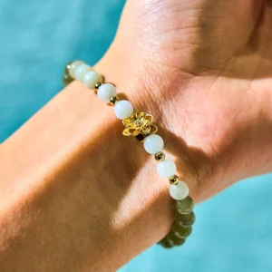 Hetian jade lotus abundance bracelet worn on left wrist, showing gradient white to green jade beads with gold lotus charm against blue fabric