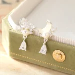 Hetian jade lotus and crescent moon sterling silver drop earrings on green velvet jewelry box, showcasing handcrafted nephrite with cubic zirconia and pearl accents