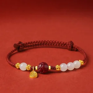 24K gold plated Hetian white jade lotus bracelet with red string and cinnabar bead on dark red background