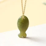Hand-carved Hetian jade lucky fish pendant with delicate gold-toned chain, close-up front view showing intricate carving details and rich green color
