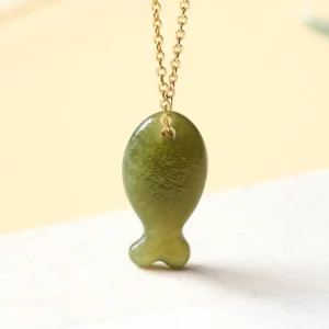 Hand-carved Hetian jade lucky fish pendant with delicate gold-toned chain, close-up front view showing intricate carving details and rich green color