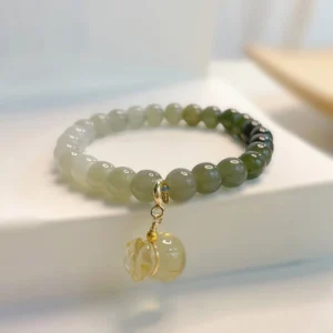 Hetian jade money bag charm bracelet overhead view showing gradient green beads with citrine money bag pendant and gold hardware