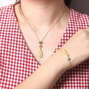 Woman wearing white jade teardrop necklace and matching adjustable jade bracelet with gold-plated enamel details in everyday outfit