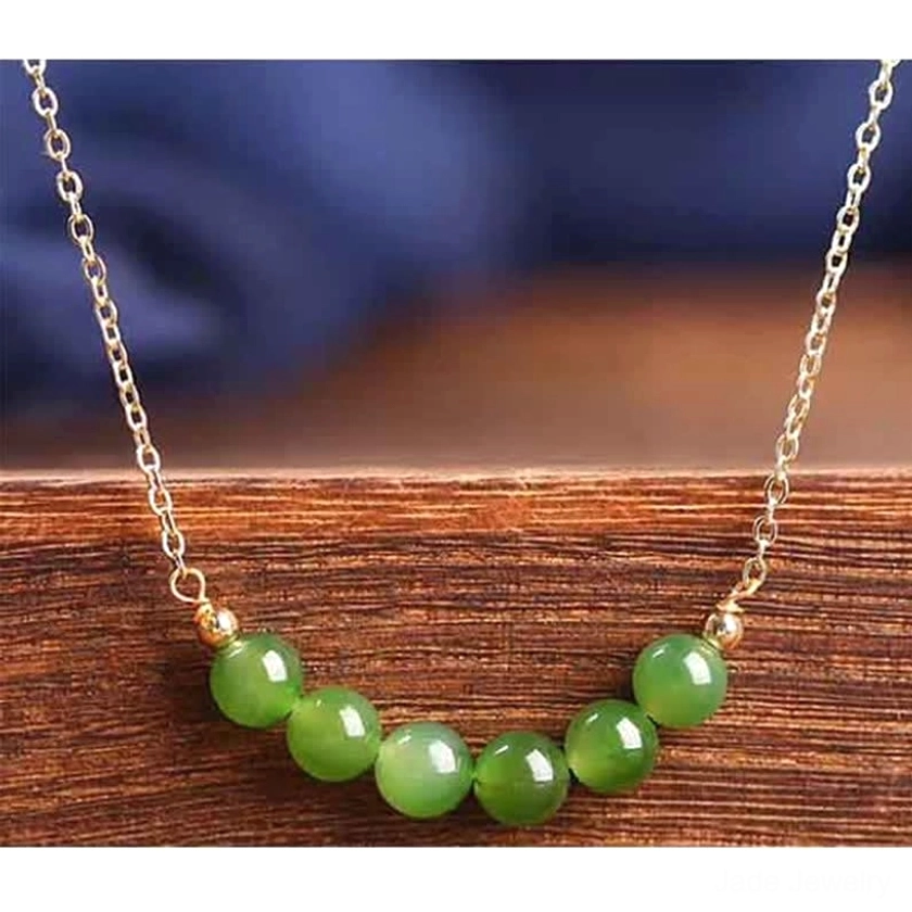 Oblique side angle view of Hetian cyan jade necklace with elegant gold-toned chain featuring seven green jade beads on polished wood table surface - jade necklace side styling view