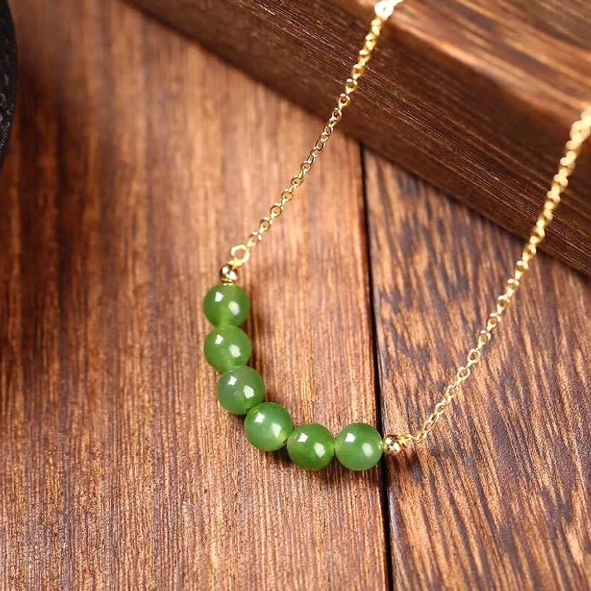 Three-quarter oblique side view of Hetian cyan jade necklace featuring elegant green jade bead pendant on gold-plated chain against wood grain texture - side angle jewelry photography