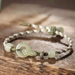 Hetian jade peace buckle braided bracelet with adjustable sizing options displayed on wooden surface, showing interlocking jade rings and metal spacer beads