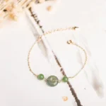 Hetian jade peace buckle bracelet with gold chain displayed on traditional Chinese ink wash background, featuring central jade buckle and two small jade beads