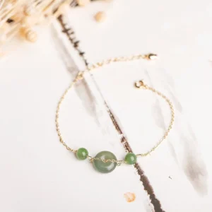 Hetian jade peace buckle bracelet with gold chain displayed on traditional Chinese ink wash background, featuring central jade buckle and two small jade beads