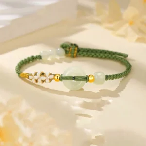 Hetian jade peace buckle bracelet with pale green jade and green braided cord, displayed on warm floral backdrop with gold accents