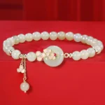 Hetian jade peace buckle bracelet with peach blossom charm on red fabric, flat lay view showing jade beads and gold flower details
