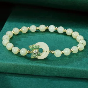 Hetian jade peace buckle bracelet with butterfly charm on dark velvet - overhead view showing jade beads and silver spacers