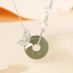 Hetian jade peace buckle butterfly silver necklace with green jade pendant and sterling silver chain on warm background