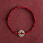 Dark red braided Hetian jade peace buckle bracelet with woven cord on maroon background
