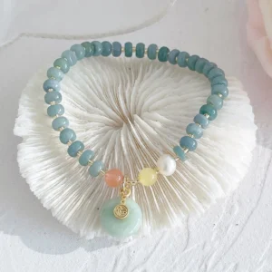 Hetian jade teal beads with light green peace buckle fu character charm on white shell coaster, top view