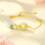 Gold-plated Hetian jade peace buckle bracelet with peach blossom charm and natural jade beads, flat lay top-down view on floral background