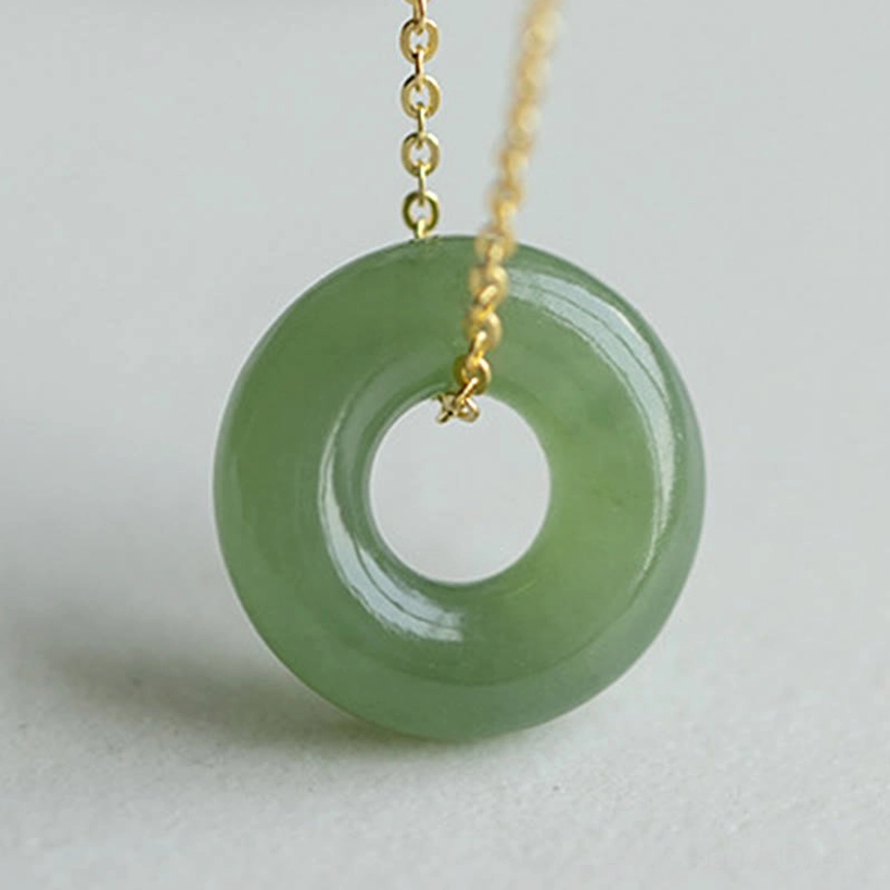 Large close-up detail of thick smooth Hetian jade peace buckle pendant with gold chain connector on neutral studio background