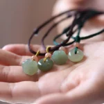 Hetian jade peace buckle and lotus pendant necklaces in brown and green wax cord, overhead close-up on palm display