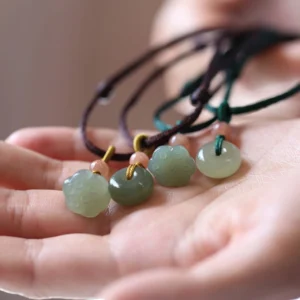 Hetian jade peace buckle and lotus pendant necklaces in brown and green wax cord, overhead close-up on palm display