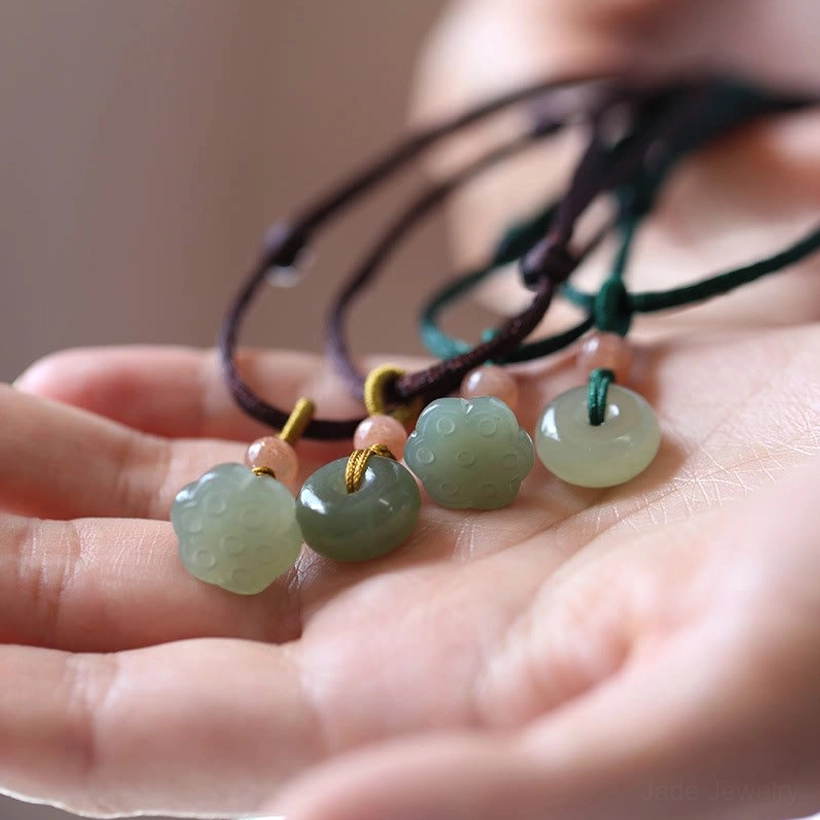 Hetian jade peace buckle and lotus pendant necklaces in brown and green wax cord, overhead close-up on palm display