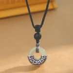 Hetian jade peace buckle pendant necklace with black obsidian bead and sterling silver, front close-up view on light background