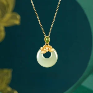 Hetian jade lotus peace buckle necklace pendant with 925 sterling silver gold-plated chain, overhead close-up view on dark teal background with golden leaf accents