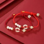 Red string Hetian jade peace buckle bracelets with pearls and silver accents displayed on textured background