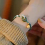 Hetian jade peace buckle bracelet with pearls worn on wrist with gold lotus charm and green braided cord