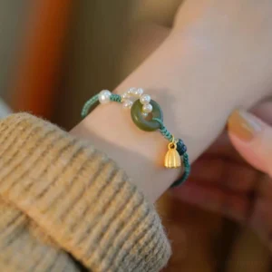Hetian jade peace buckle bracelet with pearls worn on wrist with gold lotus charm and green braided cord