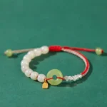 Hetian jade peace buckle bracelet with red cord and silver charm on dark green background
