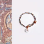 Hetian jade peace buckle bracelet with multicolor braided rope displayed on ancient Chinese mural art background