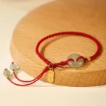 Hetian jade peace buckle red string protection bracelet overhead view showing light green jade disc with gold charm and tassel detail