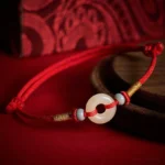 Hetian jade peace buckle red string bracelet with gold woven accents and ceramic beads on vintage fabric background