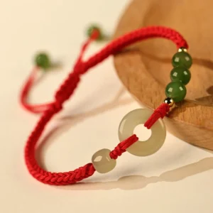 Red string Hetian jade peace buckle bracelet with adjustable cord fastener, close-up overhead view on wooden surface