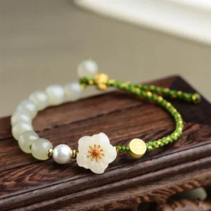 Hetian jade peach blossom bracelet with green woven cord and white floral charm, overhead flat lay on wooden stand