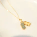 Hetian jade peanut pendant necklace with sterling silver chain, front flat lay view showcasing gold-tone peanut design and light green jade beads