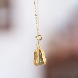 Open peanut jade pendant close-up, displaying embedded light green Hetian jade stone inside golden casing with spring clasp mechanism