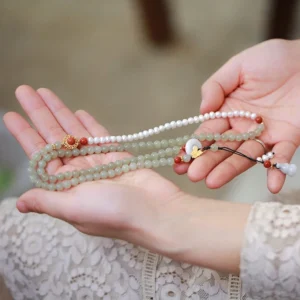 Hetian jade and pearl beaded bracelet with butterfly charm, overhead view showing light green jade beads, white pearl accents, and gold-plated charms on elastic cord