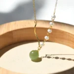 Hetian jade pearl necklace with light green jade bead and white pearls on gold chain, flat lay on wooden tray