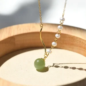 Hetian jade pearl necklace with light green jade bead and white pearls on gold chain, flat lay on wooden tray