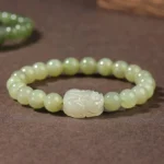 Hetian jade Pixiu prosperity bracelet flat lay with carved white Pixiu charm centerpiece and light green jade beads