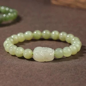 Hetian jade Pixiu prosperity bracelet flat lay with carved white Pixiu charm centerpiece and light green jade beads