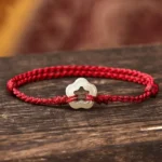 Hetian jade plum blossom red string bracelet side view on dark wooden surface with braided cord and hollow jade charm