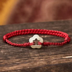 Hetian jade plum blossom red string bracelet side view on dark wooden surface with braided cord and hollow jade charm
