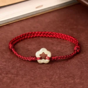 Hetian jade plum blossom bracelet top-down view on brown suede desk showing intricate braided red cord and flower-shaped jade pendant